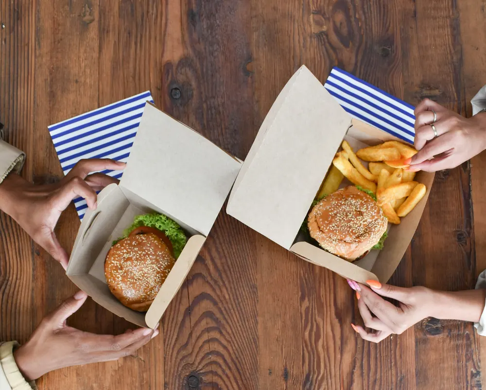 Hambúrgueres e batatas servidos em caixas de papel para delivery